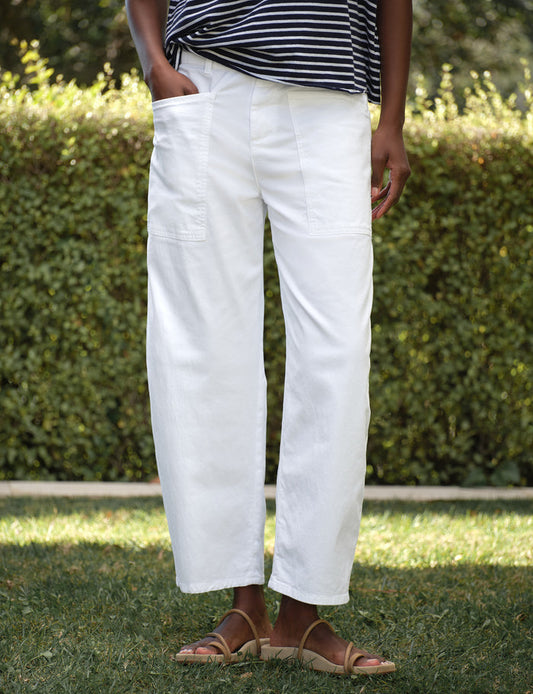 Person wearing white pants and a striped shirt standing outdoors with greenery in the background