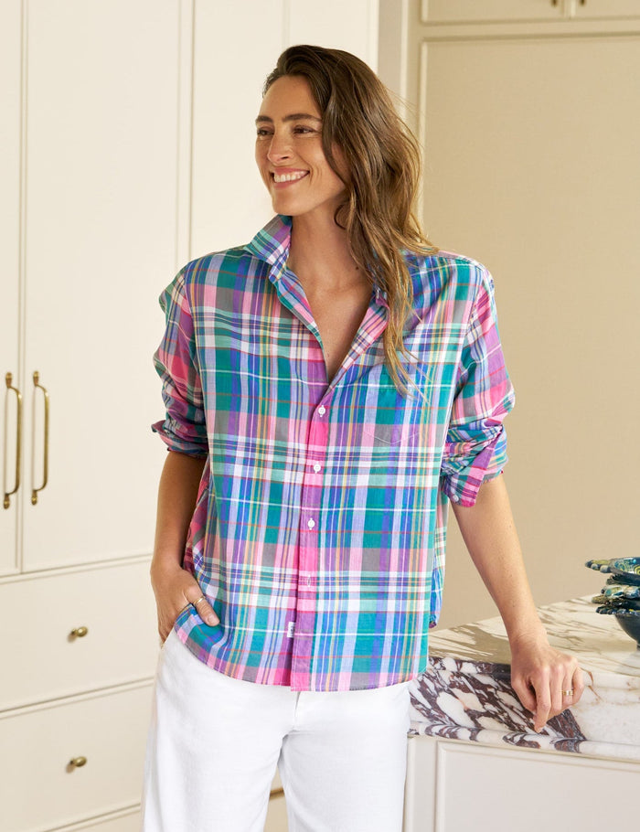 Woman wearing a colorful plaid shirt and white pants in a kitchen.