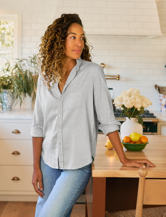 Woman standing in a kitchen wearing a light gray button-up shirt and blue jeans.
