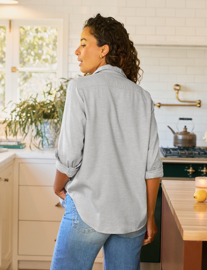 Woman standing in a kitchen wearing a light gray shirt and blue jeans.