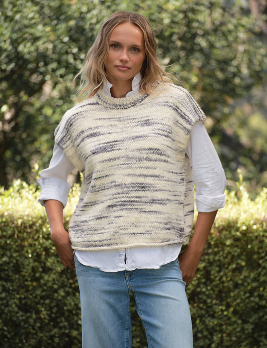 Woman wearing a patterned vest over a white shirt with blue jeans outdoors.