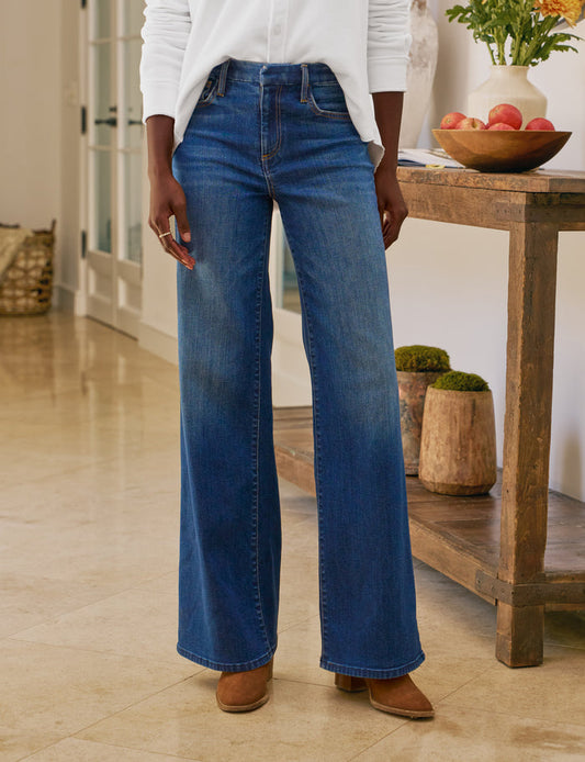 Person wearing blue jeans standing in a room with wooden furniture and decor.
