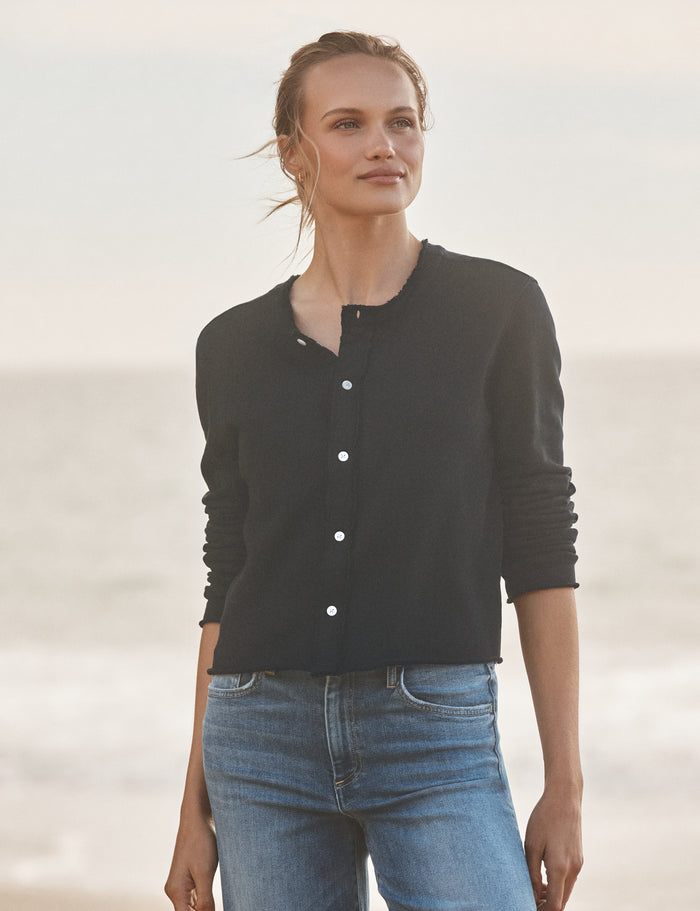 Woman wearing a navy cardigan and blue jeans standing against a light background