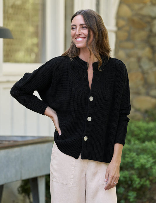 Woman wearing a black cardigan with white buttons outdoors.