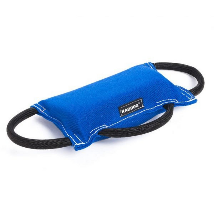 Bright royal blue padded dog training bite tug with a smooth fabric surface, white stitching along the edges, and two black rope handles on each side, featuring a small brand label, displayed against a light background.