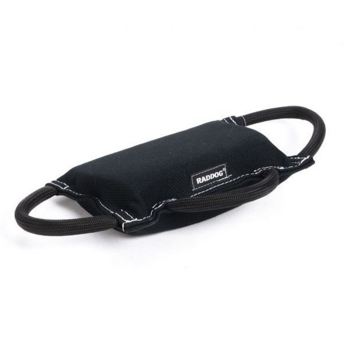 Black padded dog training bite tug with a textured fabric surface, white stitching along the edges, and two black rope handles on each side, featuring a small brand label, displayed against a light background.