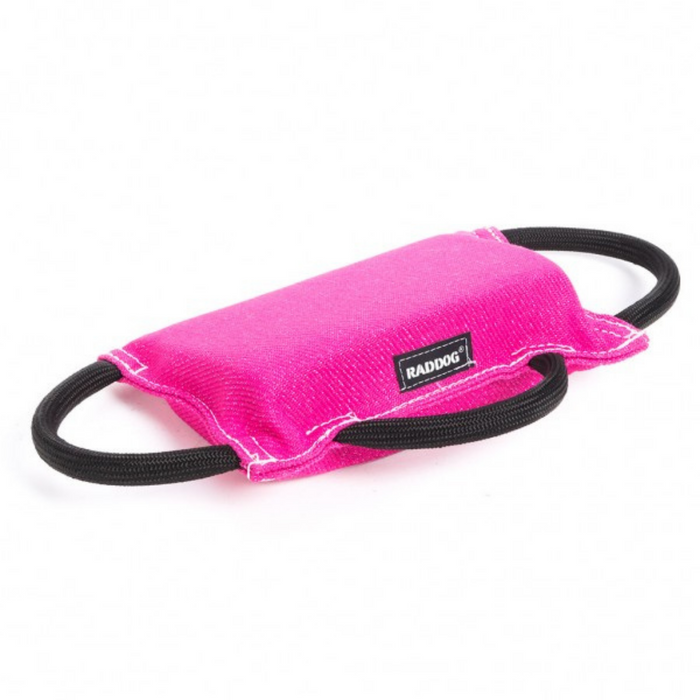 Hot pink padded dog training bite tug with a textured fabric surface, white stitching along the edges, a black “RADDOG” label on the side, and two black rope handles on each end, displayed against a light background.