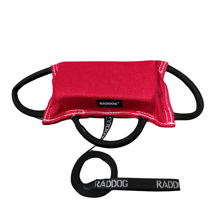 Red dog training bite pad made from durable fabric, featuring reinforced stitching, multiple black loop handles, and a RADDOG logo label, displayed on a white background.