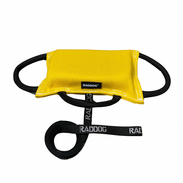 Yellow dog training bite pad made from durable fabric, featuring reinforced stitching, multiple black loop handles, and a RADDOG logo label, displayed on a white background.
