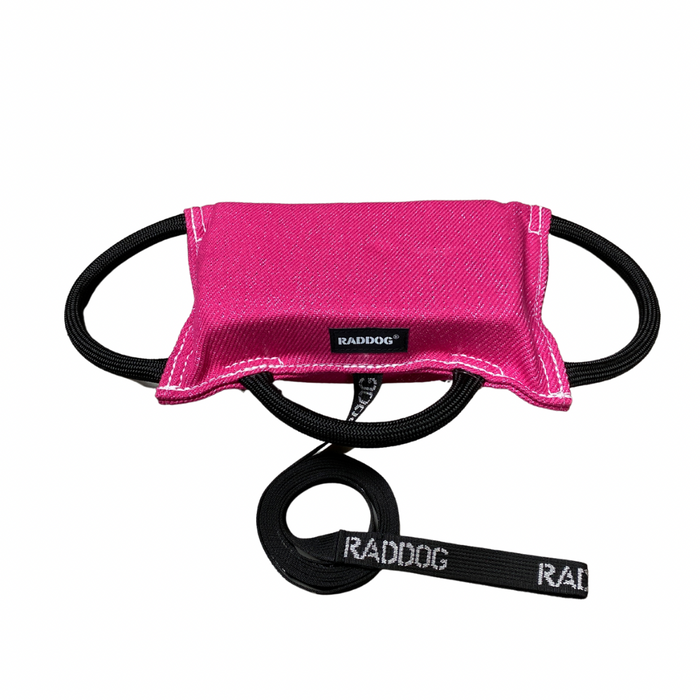 Pink dog training bite pad made from durable fabric, featuring reinforced stitching, multiple black loop handles, and a RADDOG logo label, displayed on a white background.