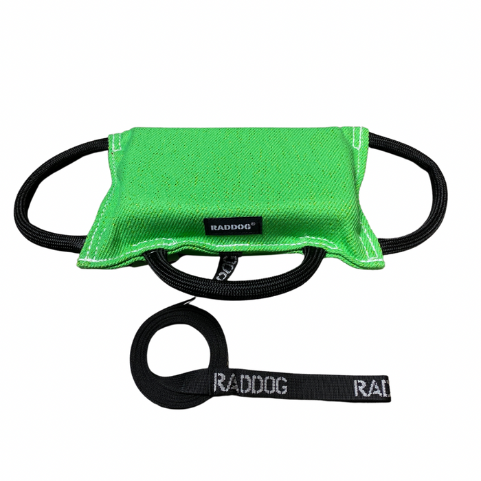 Green dog training bite pad made from durable fabric, featuring reinforced stitching, multiple black loop handles, and a RADDOG logo label, displayed on a white background.