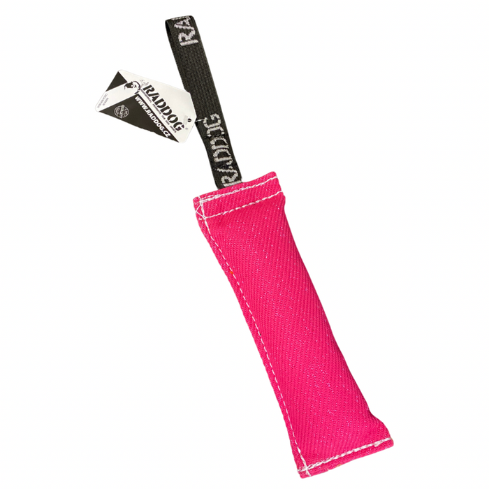 Pink dog training tug toy with a durable textured fabric bite area, reinforced white stitching, and a black loop handle labeled “RADDOG,” with a product tag attached, isolated on a white background.