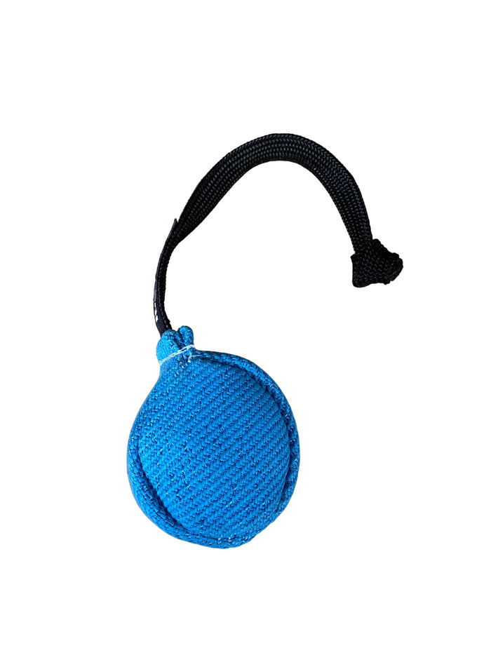Blue fabric dog training ball with a textured woven surface and a black braided rope handle, isolated on a white background.