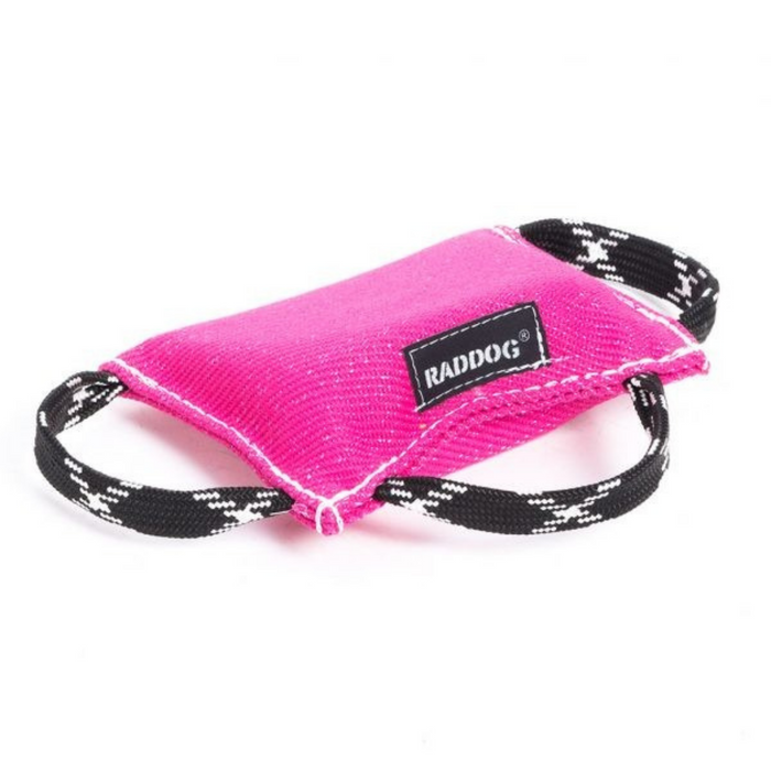 Pink dog training bite wedge made of durable textured fabric with reinforced white stitching and two black-and-white patterned handles, featuring a “RADDOG” label, isolated on a white background.