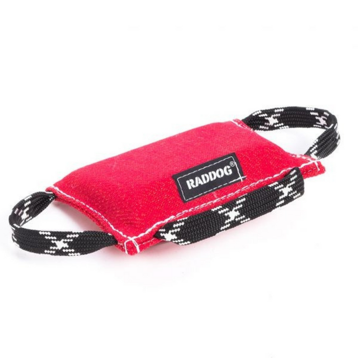 Red dog training bite wedge made of durable textured fabric with reinforced white stitching and two black-and-white patterned handles, featuring a “RADDOG” label, isolated on a white background.