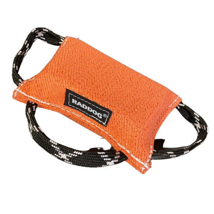 Orange dog training bite wedge made of durable textured fabric with reinforced white stitching and two black-and-white patterned handles, featuring a “RADDOG” label, isolated on a white background.