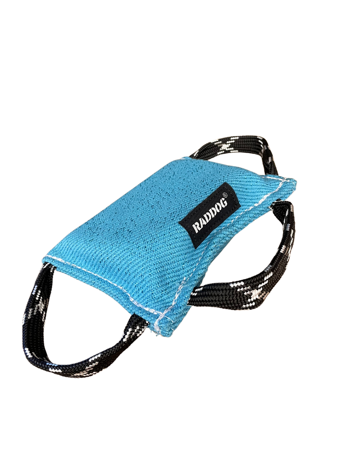 Blue dog training bite pad made of durable textured fabric with reinforced white stitching and two black-and-white patterned handles, featuring a “RADDOG” label, isolated on a black background.
