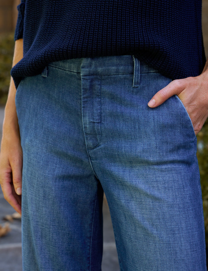 Close-up of a person wearing blue denim pants with a dark navy ribbed knit top, standing outdoors with one hand in the pocket.